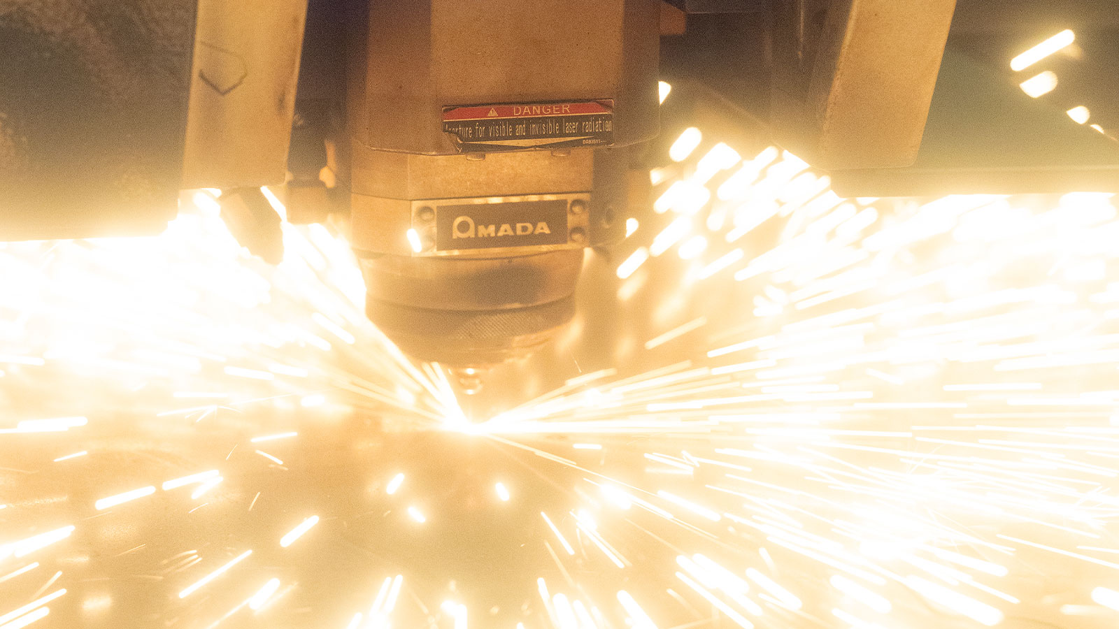 ENSIS AJ Series AMADA Fiber Laser with sparks flying during a cut.